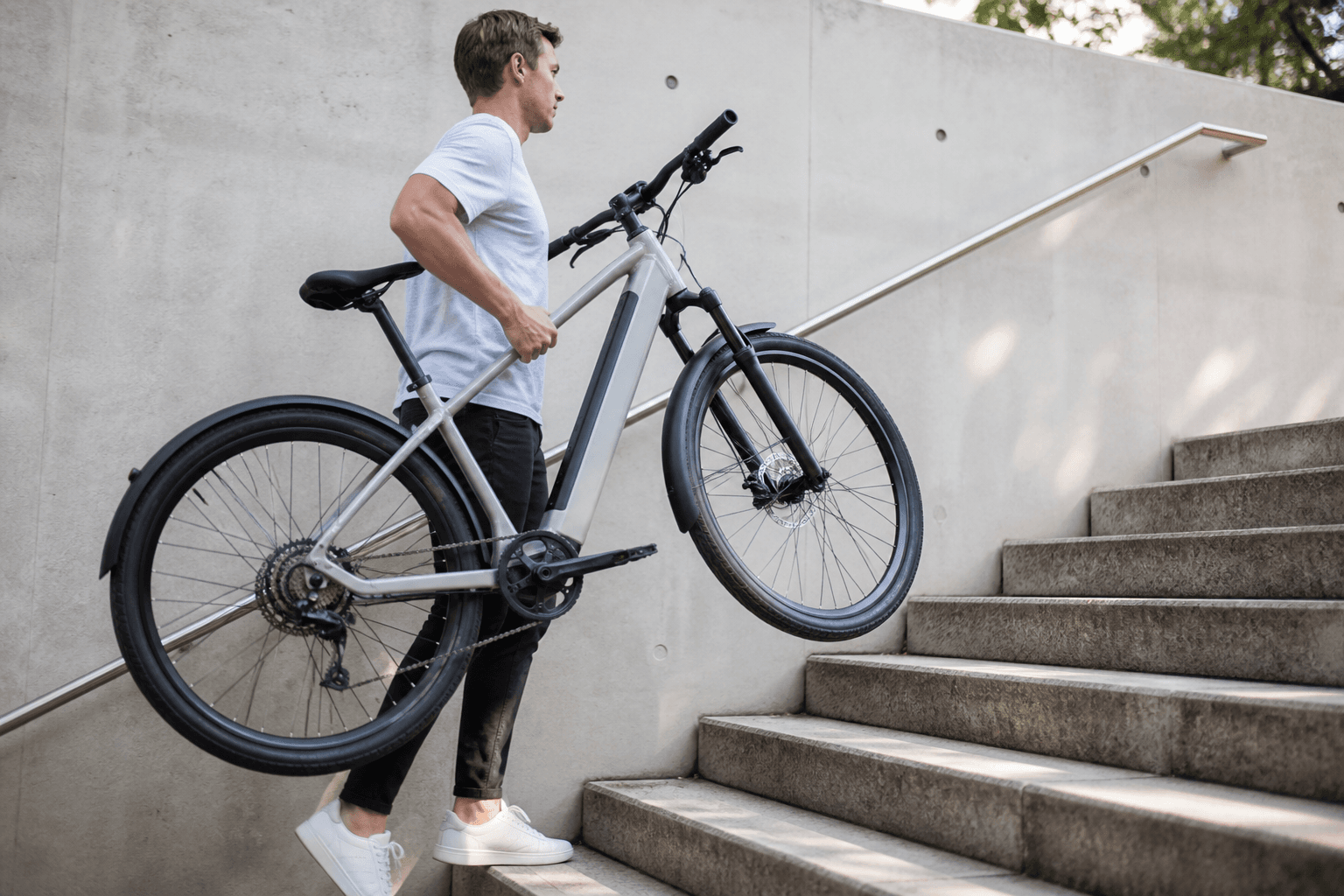 A person lifting a lightweight e-bike up a flight of stairs, with the bike appearing easy to carry.