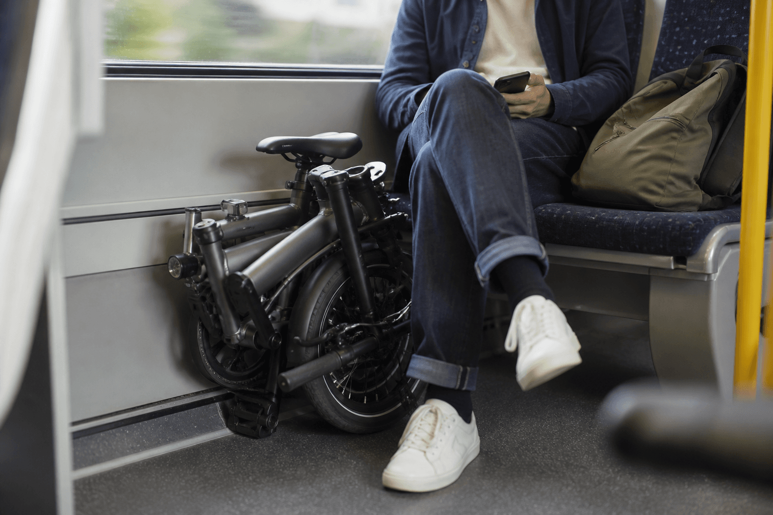 A folding e-bike folded next to a train seat, with a commuter's bag nearby.